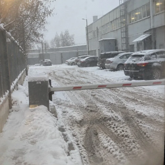 Снег и колеи на парковке и пешеходной дорожке у шлагбаума